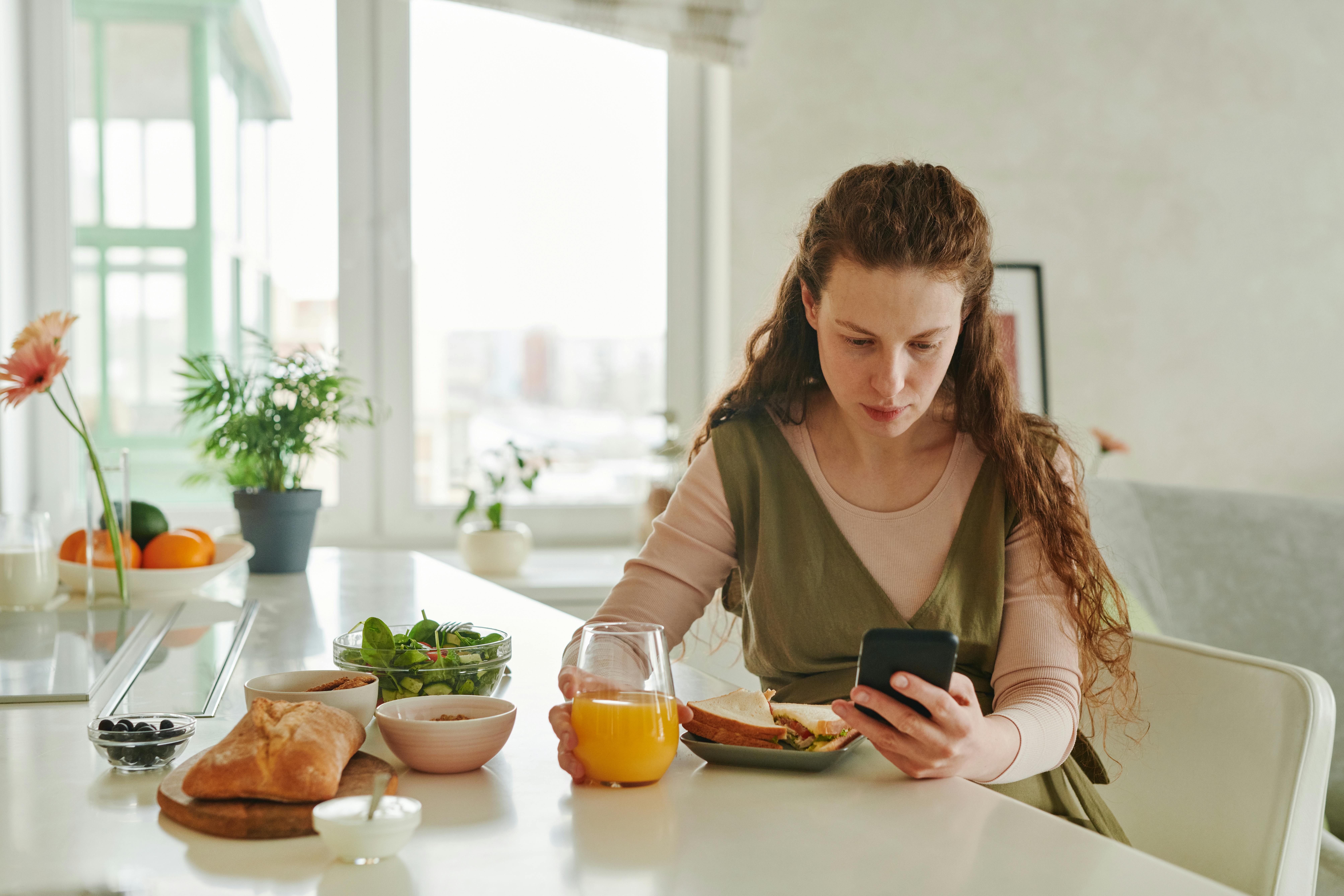 A woman eating while looking at her phone.