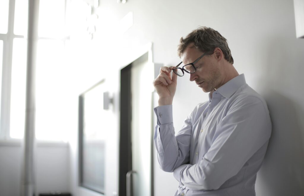 A stressed man removing his glasses from his face.