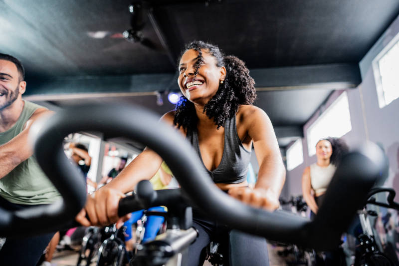 A middle-aged adult woman exercising on a stationary bike during a group class.